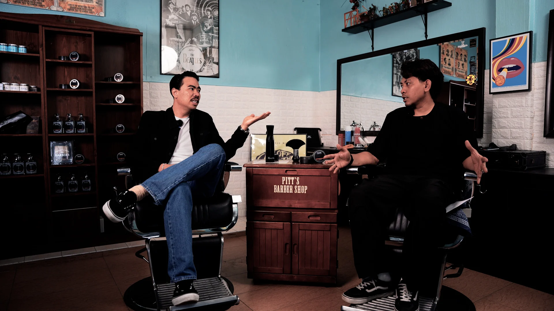 Two men sitting in barber chairs having a conversation inside Pitt’s Barber Shop, with Haestic products on the cabinet between them