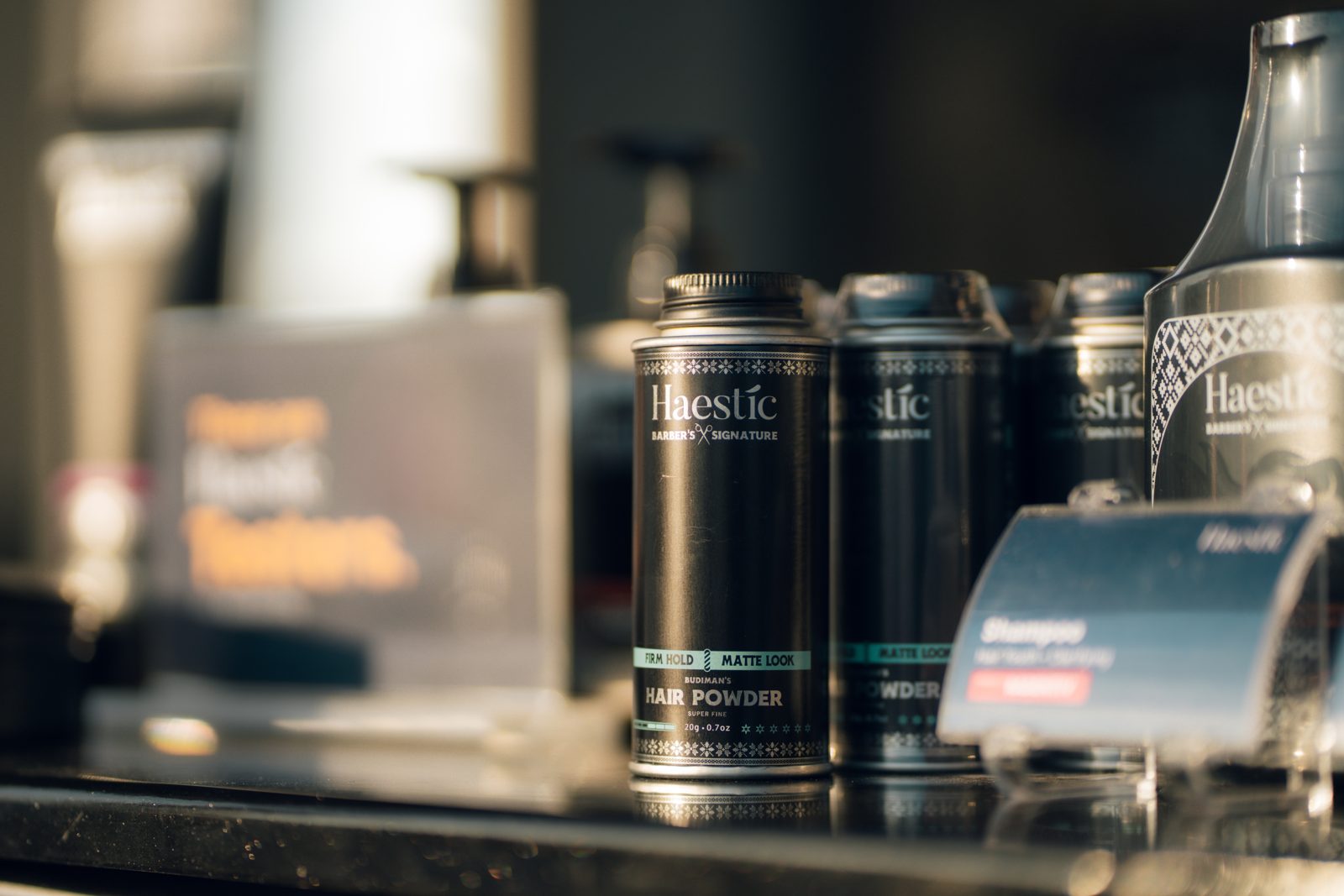 Haestic Barber's Signature Hair Powder tins on a shelf beside a shampoo display