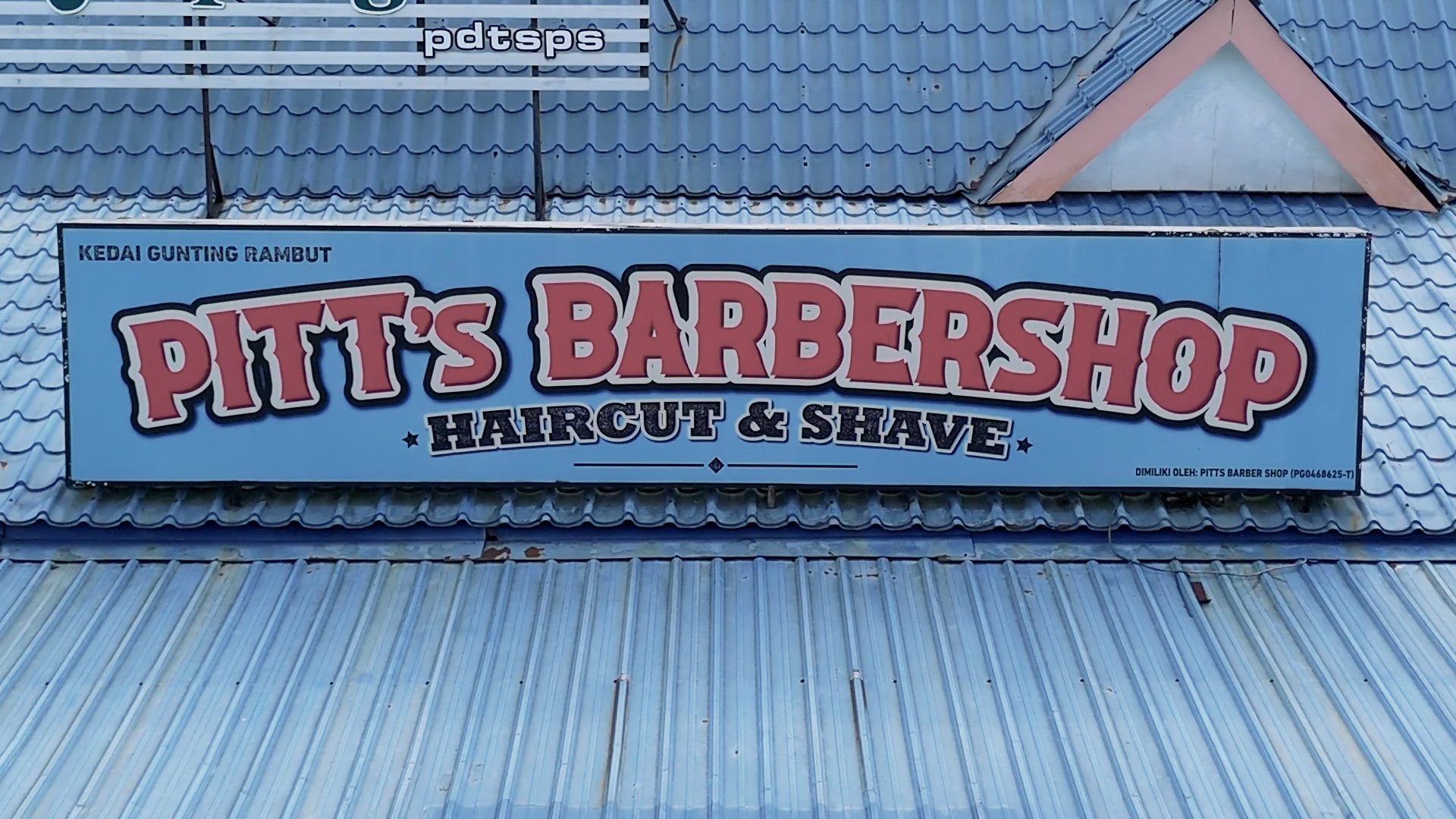 Pitt’s Barbershop Haircut & Shave signboard above a blue roof