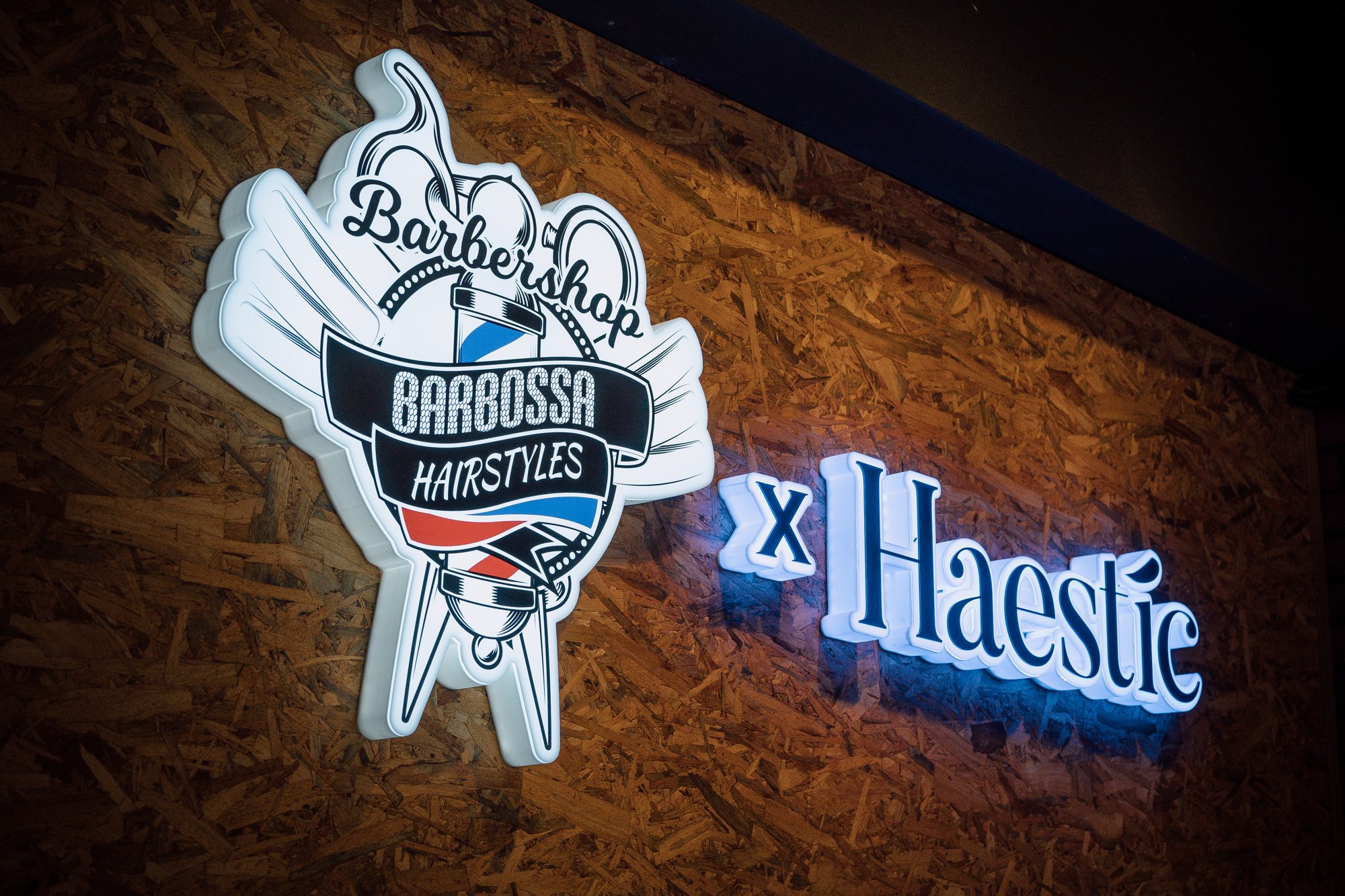 Barbossa Barbershop Hairstyles x Haestic illuminated sign on a wood-chip wall